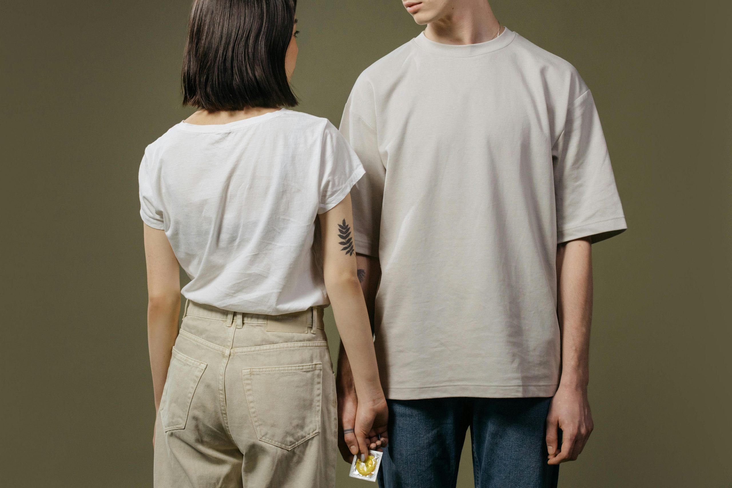A couple stands closely, discreetly holding a condom, promoting safe sex awareness in a minimalist setting.